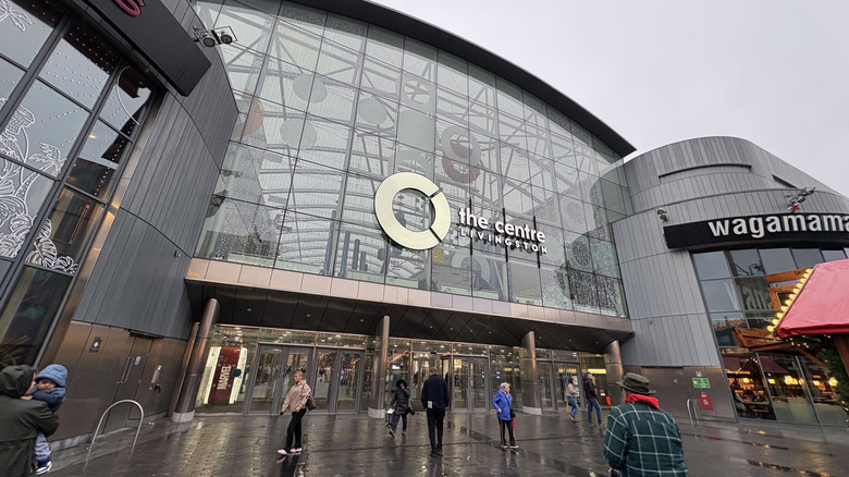 A view from below of modern exterior of  The Centre, Livingston as people enter and exit on a cloudy, rainy day in Livingston, Scotland
