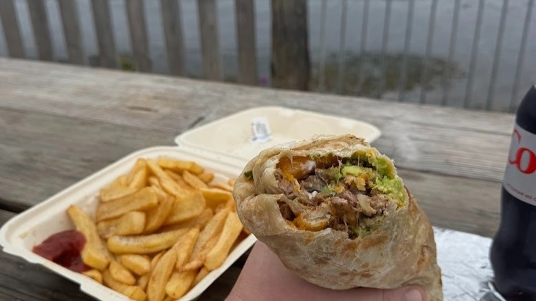A hand holds a huge carne asada breakfast burrito overlooking the ocean in Santa Cruz.