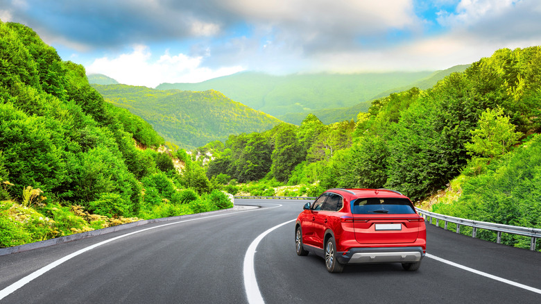 Red car driving on a road through the woods