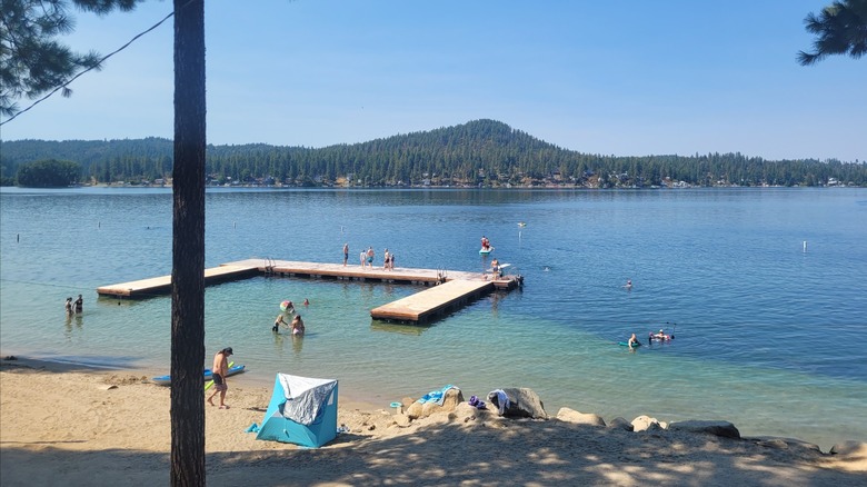 A wooden pier extending into the crystal-clear lake, with people swimming and gathering around the beach at Granite Point Resort, Loon Lake, Washington