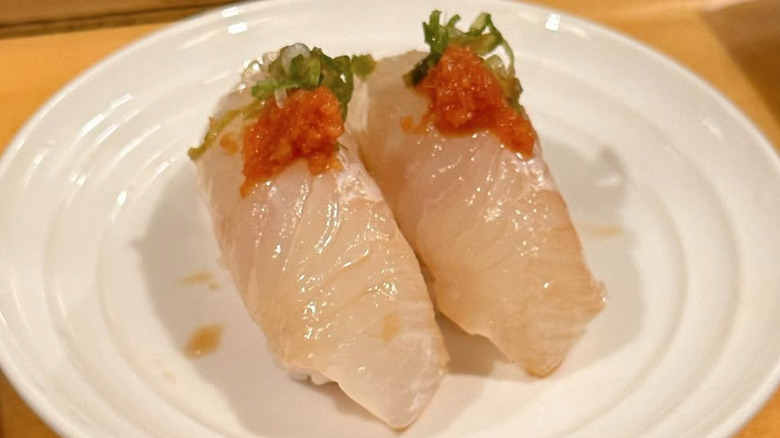 Two pieces of light colored and garnished sushi on a white plate