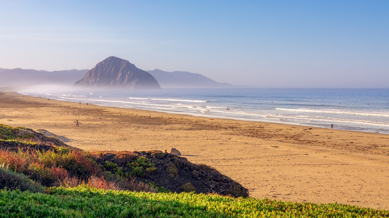 Golden sands, waves, and Morro Rock in low-lying mist in Morro Bay on the Californian coast