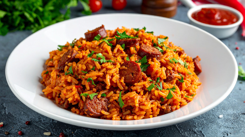 Louisiana jambalaya with rice and sausage served in a white plate, tomato sauce in the background