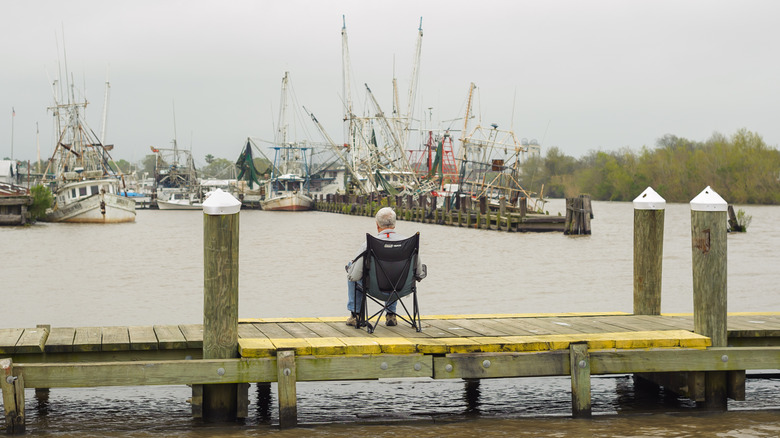 Person sits on a fishing pier with shrimp boats in view