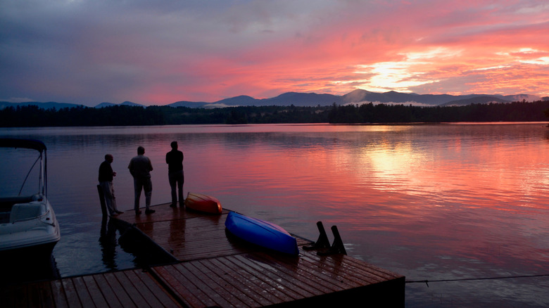 Three men standing on a dock watching the sunset near a kayak at Kezar Lake in Maine