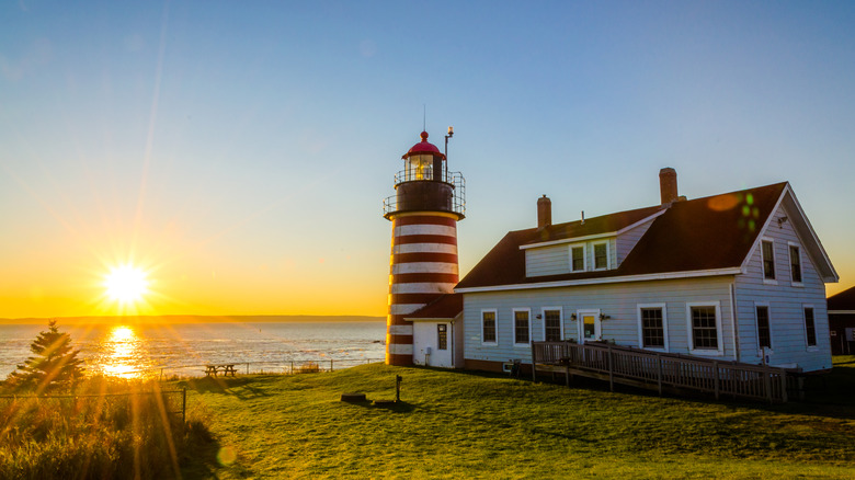 The sun rises over the ocean behind the candy-striped lighthouse at Quoddy Head