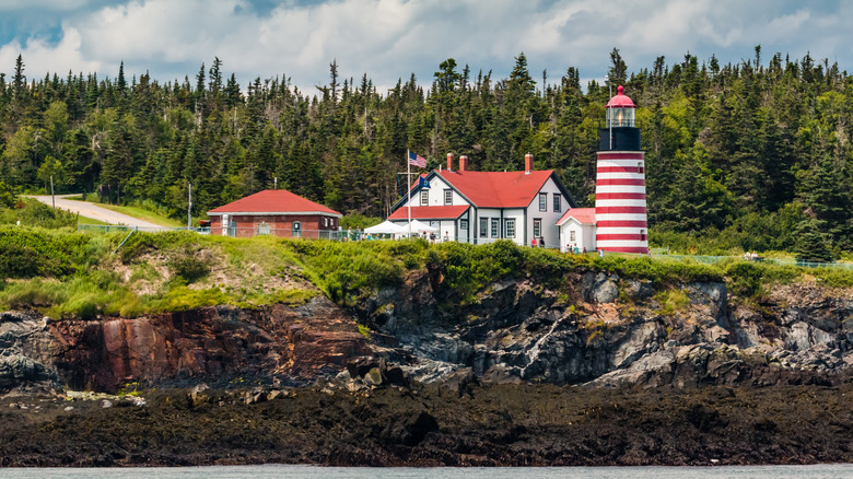 A view of the candy-striped lighthouse at Quoddy Head from the ocean, with pine forests behind it