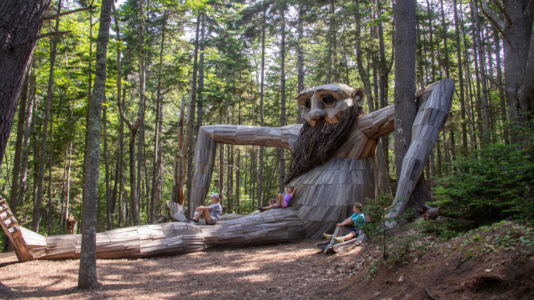 Visitors taking a break on one of the trolls in Guardians of the Seeds in Coastal Maine Botanical Gardens, Boothbay, Maine