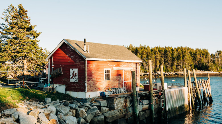 A red shack on a rocky lesge and wooden pier