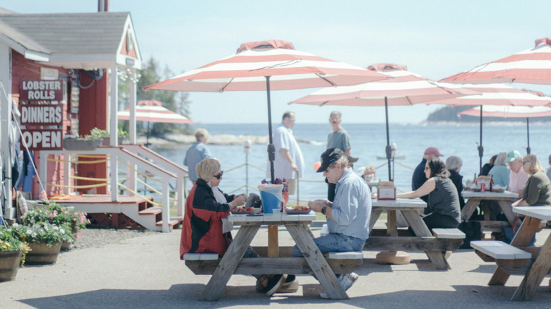 People eat seafood on wooden benches by the ocean