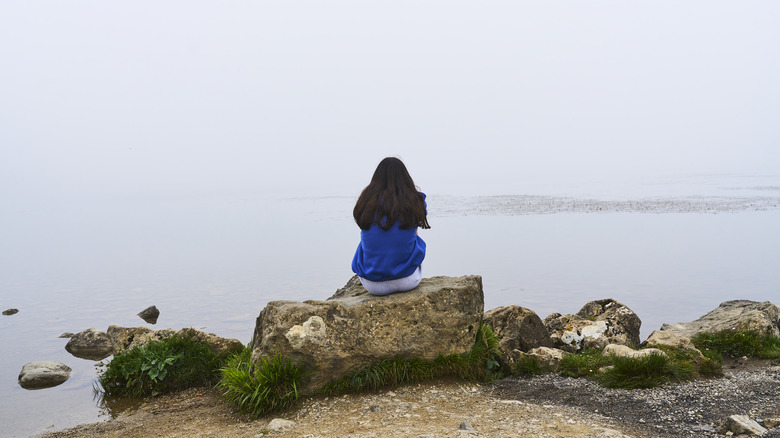 Woman sitting on rocks looking at the water
