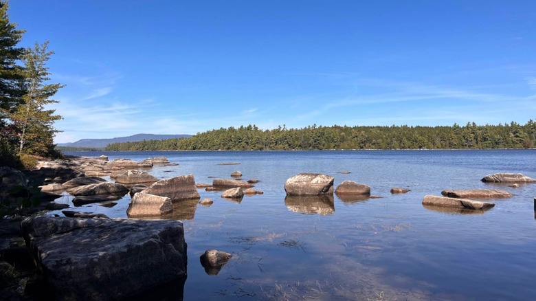 Boulders scatter throughout the calm waters of Sebec Lake in Maine, with pine trees and mountains around it.
