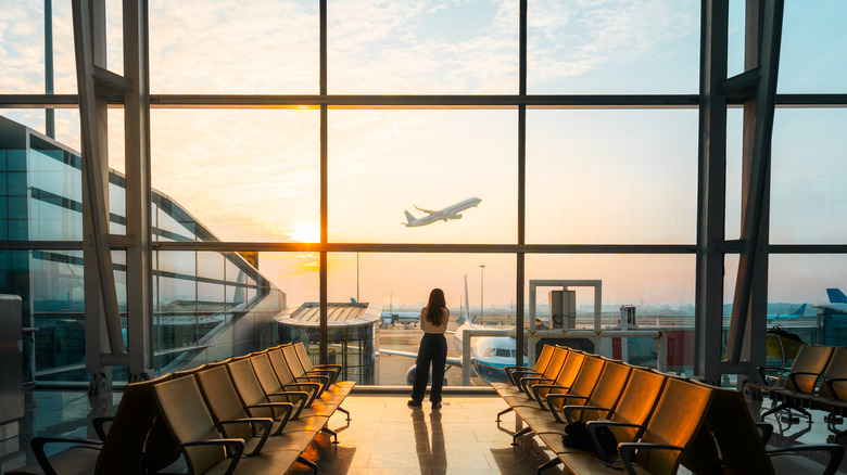 woman in silhouette watches a plane take off from inside a airport