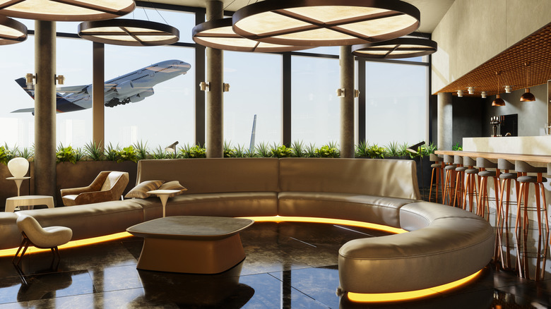 An empty airport lounge couch and bar with a plane taking off outside