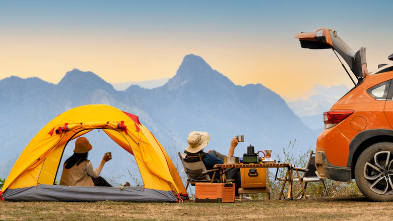 Campers enjoying a mountain view from their tent behind their car