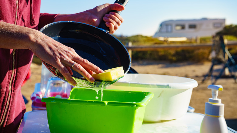 Woman washing a frying pan in a bucket at a campsite