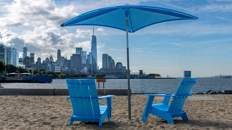 Blue Adirondack chairs and a beach umbrella on Gansevoort Peninsula looking out to NYC's skyline