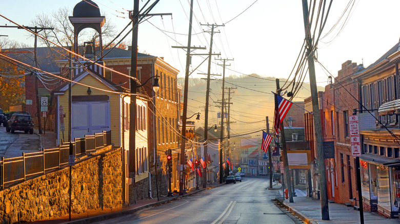 Sloping street in Ellicott City lined in brick buildings and American flags, with mountains in the background under a cloudy sky