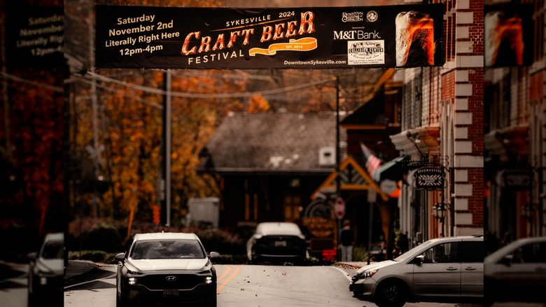 CIty street in Sykesville under a banner for the Craft Beer Festival, with autumn leaves in the background and brick buildings along the right side