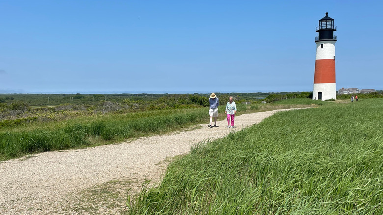 Two people walk along the path at Sankaty Head Lighthouse on Nantucket Island