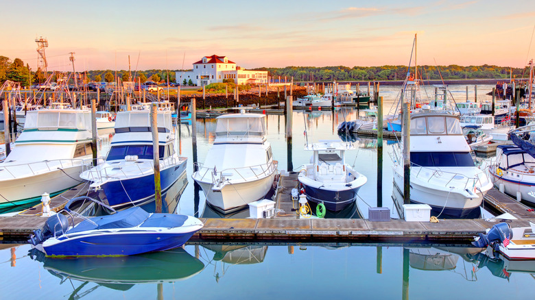 Sunset view of the marina in the Cape Cod town of Sandwich with many boats and a white structure with red roof in the background