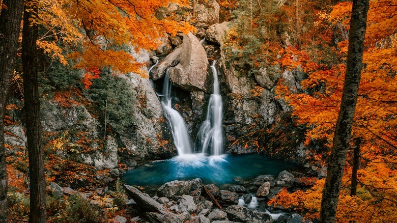 Waterfall cascades into deep blue pool surrounded by maple trees covered in orange leaves at Bash Bish Falls State Park in Massachusetts