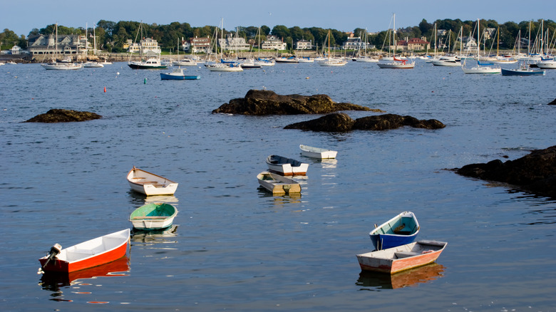 Colorful rowboats float in the foreground with sailboats in the background in Marblehead Harbor, Massachusetts.