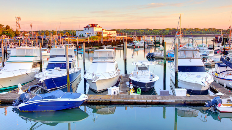 Sunset view of the marina in the Cape Cod town of Sandwich with many boats and a white structure with red roof in the background