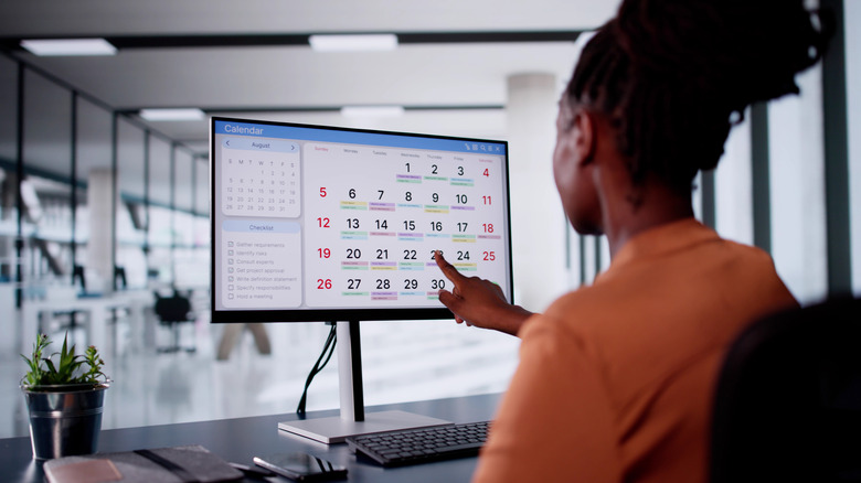 A woman in an office setting stares at her computer screen, which shows a calendar.