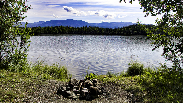 A firepit near a still lake surrounded by trees and mountains in Wrangell-St. Elias National Park