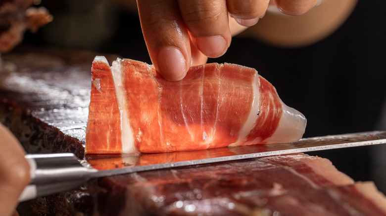 Chef cutting a thin slice of cured jamon iberico