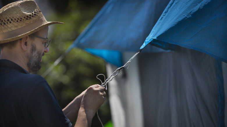 Man tying a camping knot to a tent