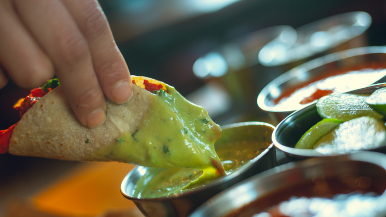 A woman dips a taco in green salsa