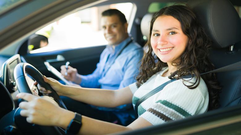 A smiling young woman takes a driver's test with an instructor