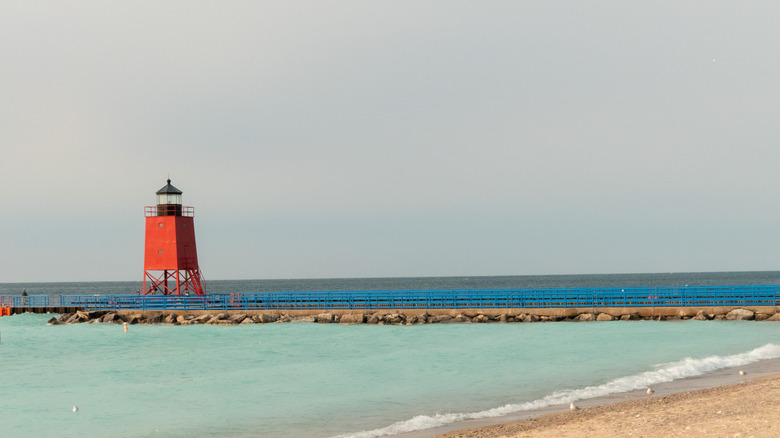 The red lighthouse atop the pier in Charlevoix, the sandy shores of Lake Michigan surrounding it
