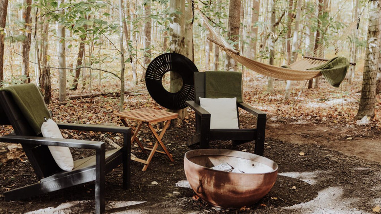 Adirondack chairs around a fire pit with a hammock behind.