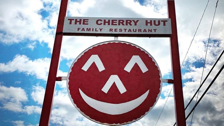 The Cherry Hut sign and smiling logo against a cloudy blue sky