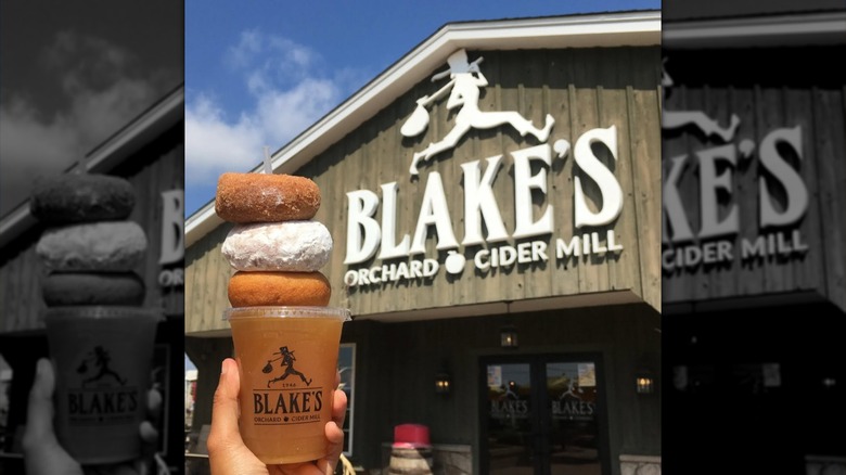 Donuts and cider held in front of Blake's Orchard sign