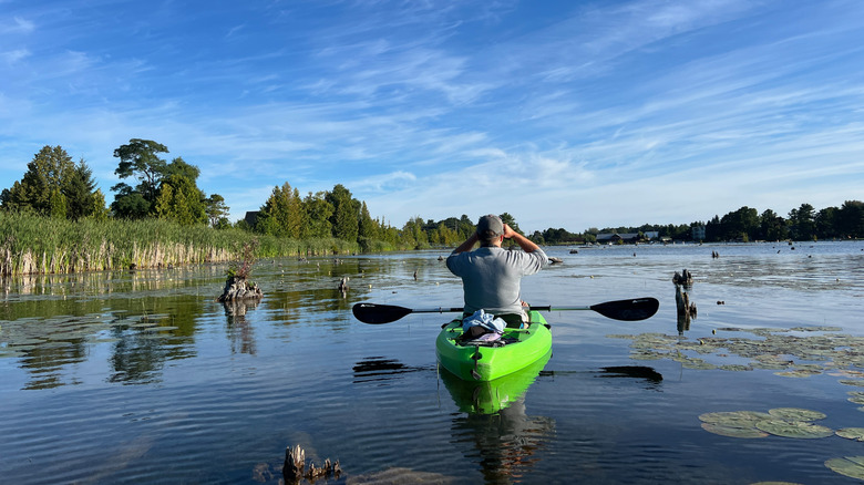 A man in a kayak birdwatching with binoculars on Elk Lake in Elk Rapids, Michigan