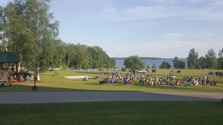 A crowd gathered on the lawn of the Erickson Center for the Arts in Curtis, Michigan with a lake in the background