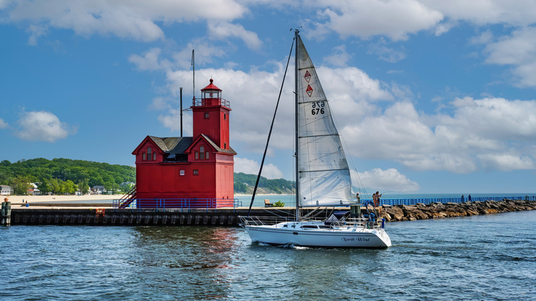 A sailboat passing the Big Red Lighthouse in Holland, Michigan on a sunny day
