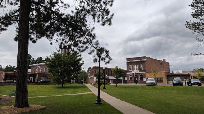 A gray summer day with a few brick buildings of downtown Gwinn seen from a grassy well-manicured park with street lights