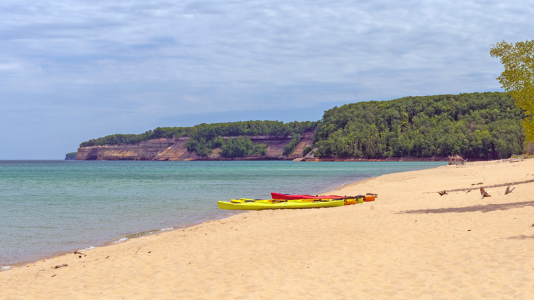 Kayaks on sandy beach overlooking Lake Superior with forested cliffs in the background and a boat on the water