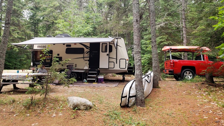 A small camper and red truck surrounded by trees in the DeTour State Forest Campground