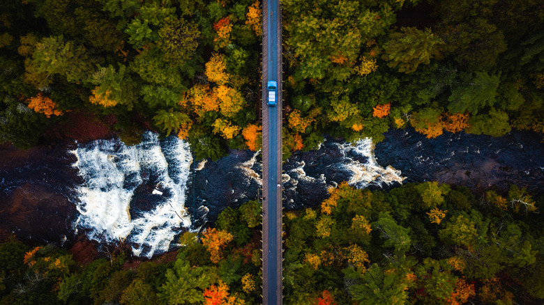Aerial view of a vehicle going over a bridge in Trout Creek, Michigan with a waterfall nearby.