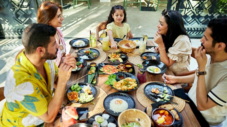 A group of smiling people enjoy platters of food at a restaurant