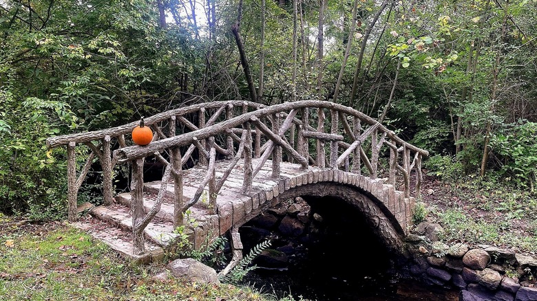 A cement bridge that crosses creek and has pumpkin on railing