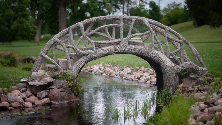 Cement bridge that looks like it's made of tree branches spans over a small creek