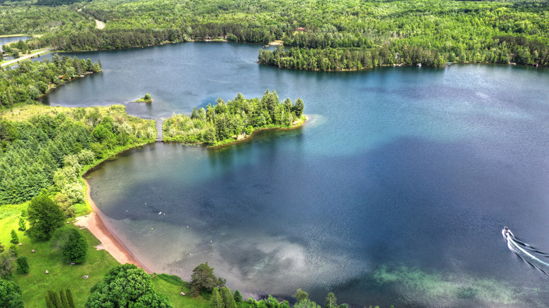 A lake with an island and beach, surrounded by trees, at Bewabic State Park