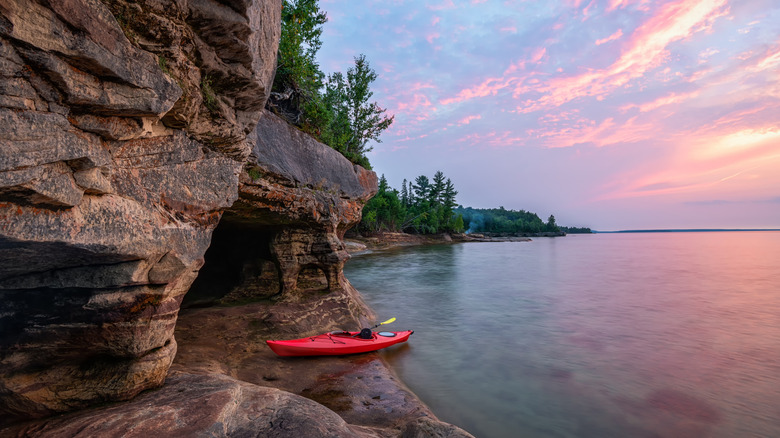 A kayak between a cave and a clear lake at sunset